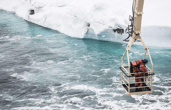 Photo. Researchers beeing transportet to an iceberg by a crane.