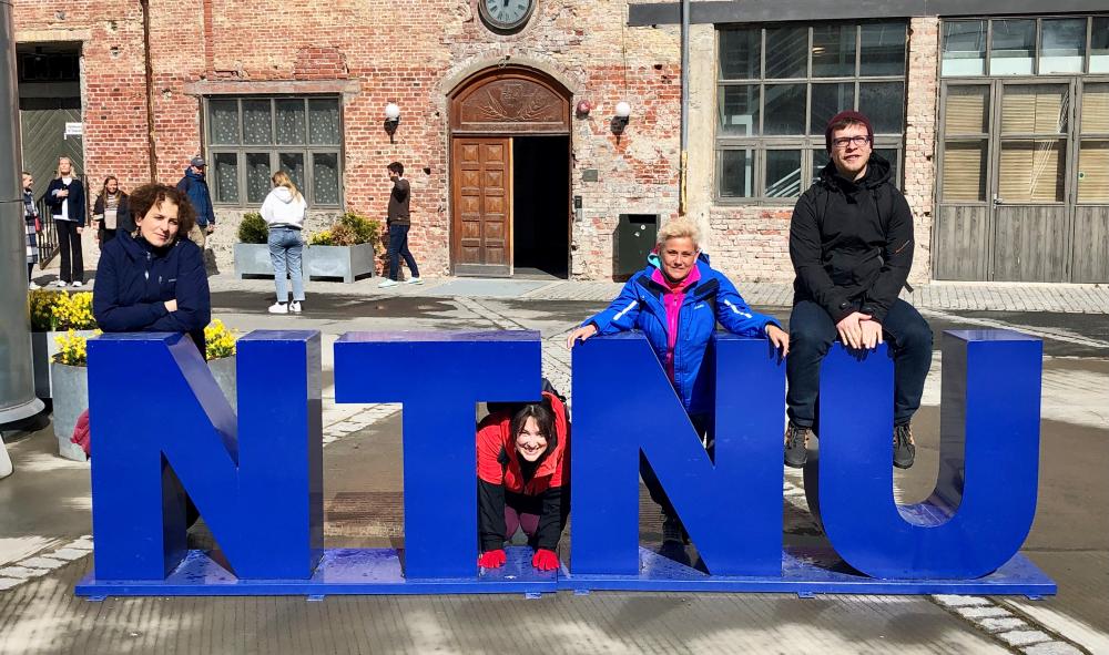 Four people surrounding the NTNU sign. Photo