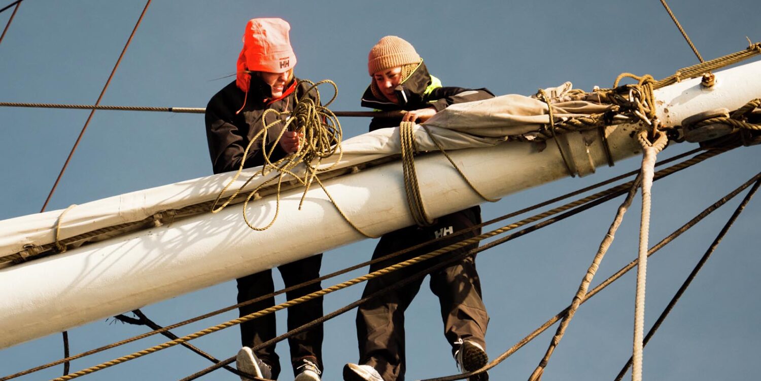 two young adults working with ropes on a big boat