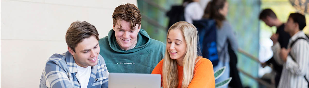 Three young adults are looking at a laptop.