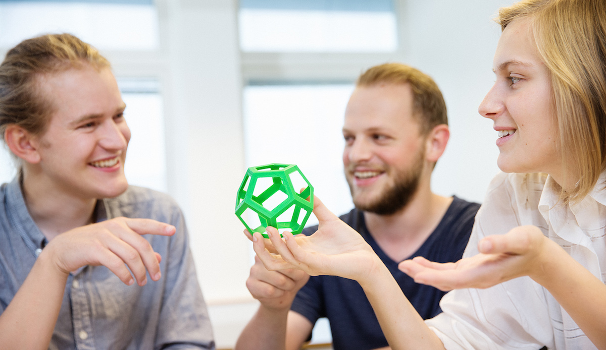 Students fascinated by a 3d-printed dodecahedron. Photo.