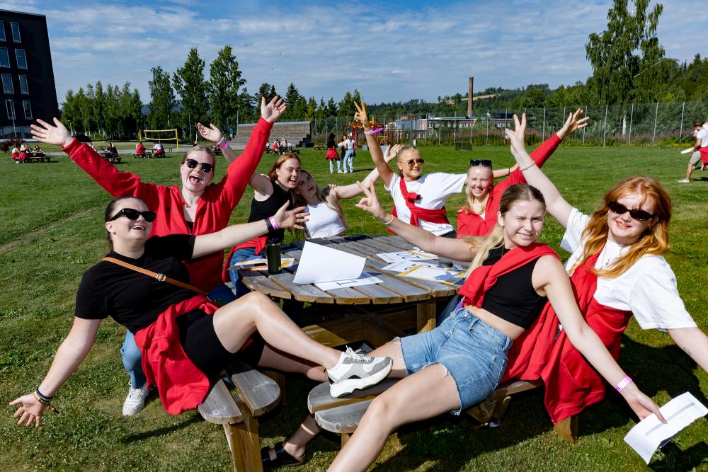 A group of students sitting on a bench, smiling, with their hands in the air