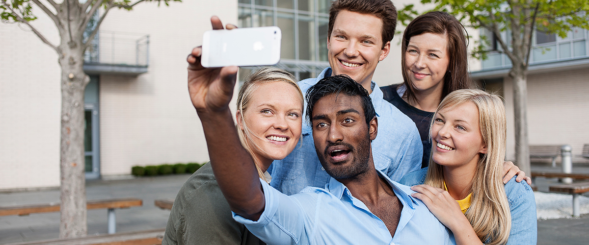 A group of students take a selfie in front of the main entrance