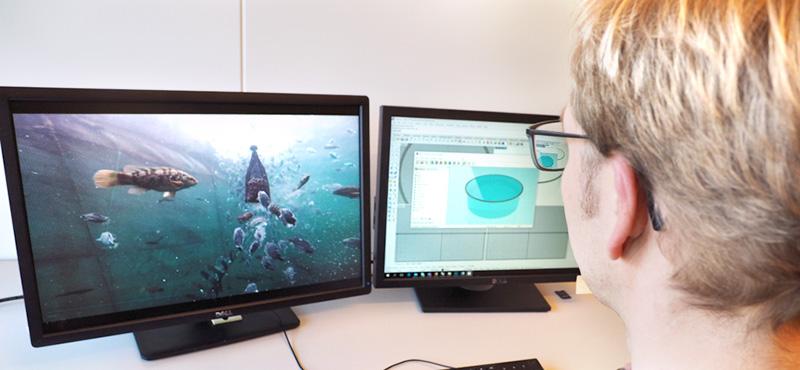 Lars Gansel in front of a computer screen with fish in a fish farm. Photo
