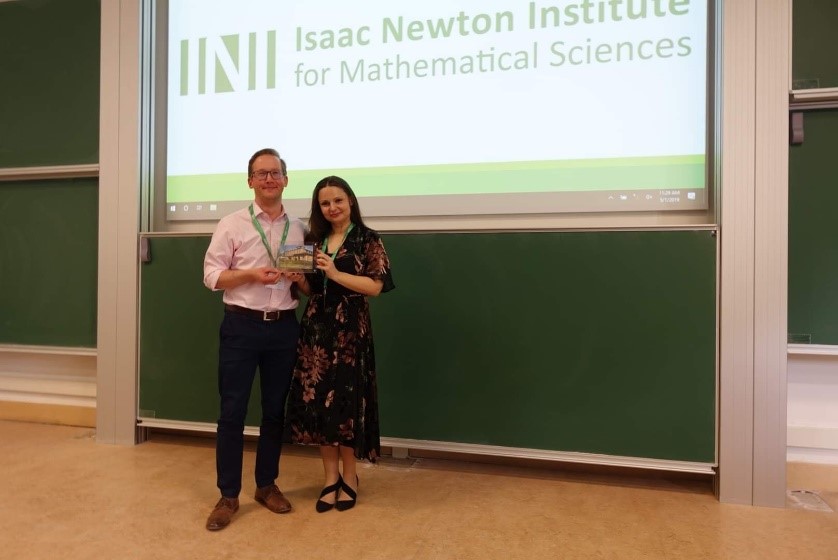 Two people standing together infront of a big screen. Photo