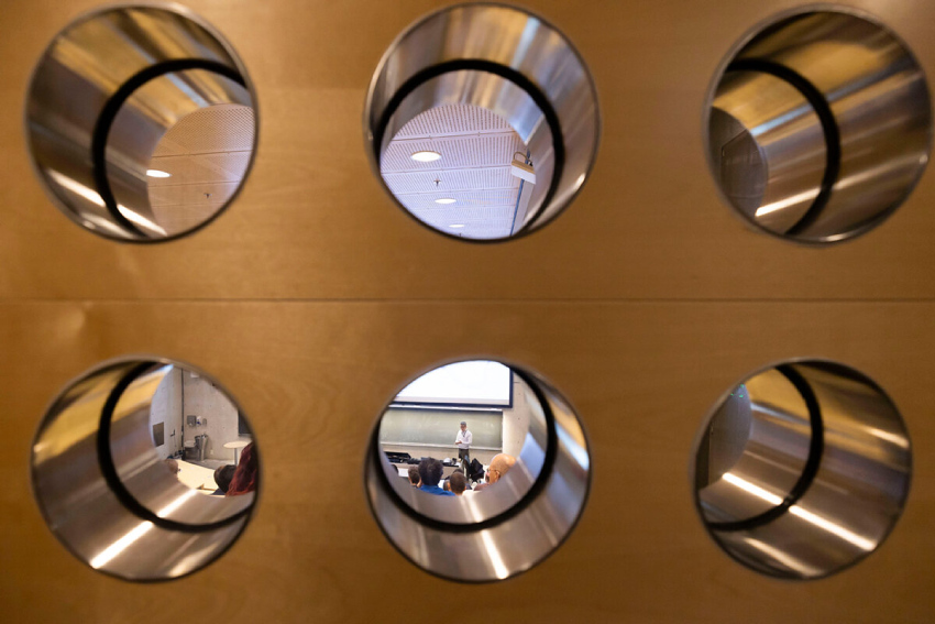 Ser gjennom seks hull i en vegg inn på en forelesningshall. Foto