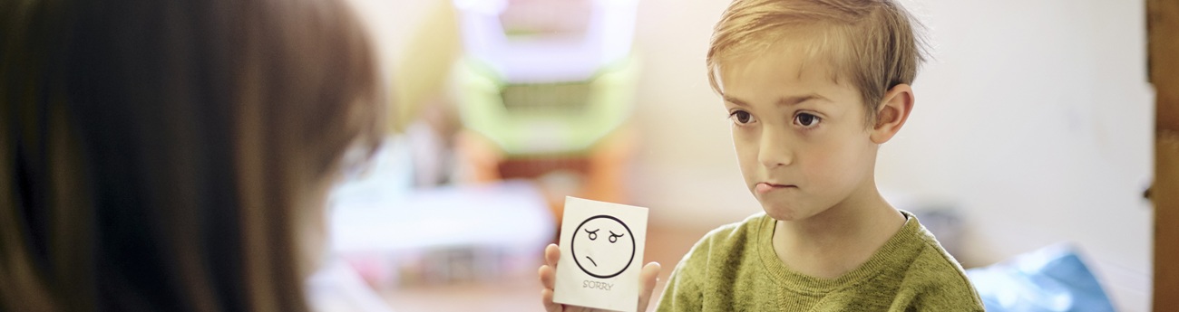 A boy shows a note with a smiley face to an adult.