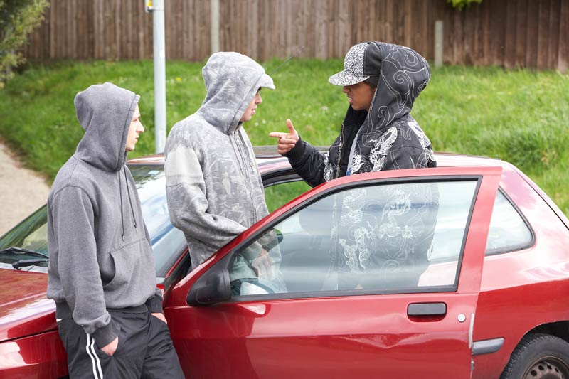 Three youths standing in front of a red car, looking at each other. photo.