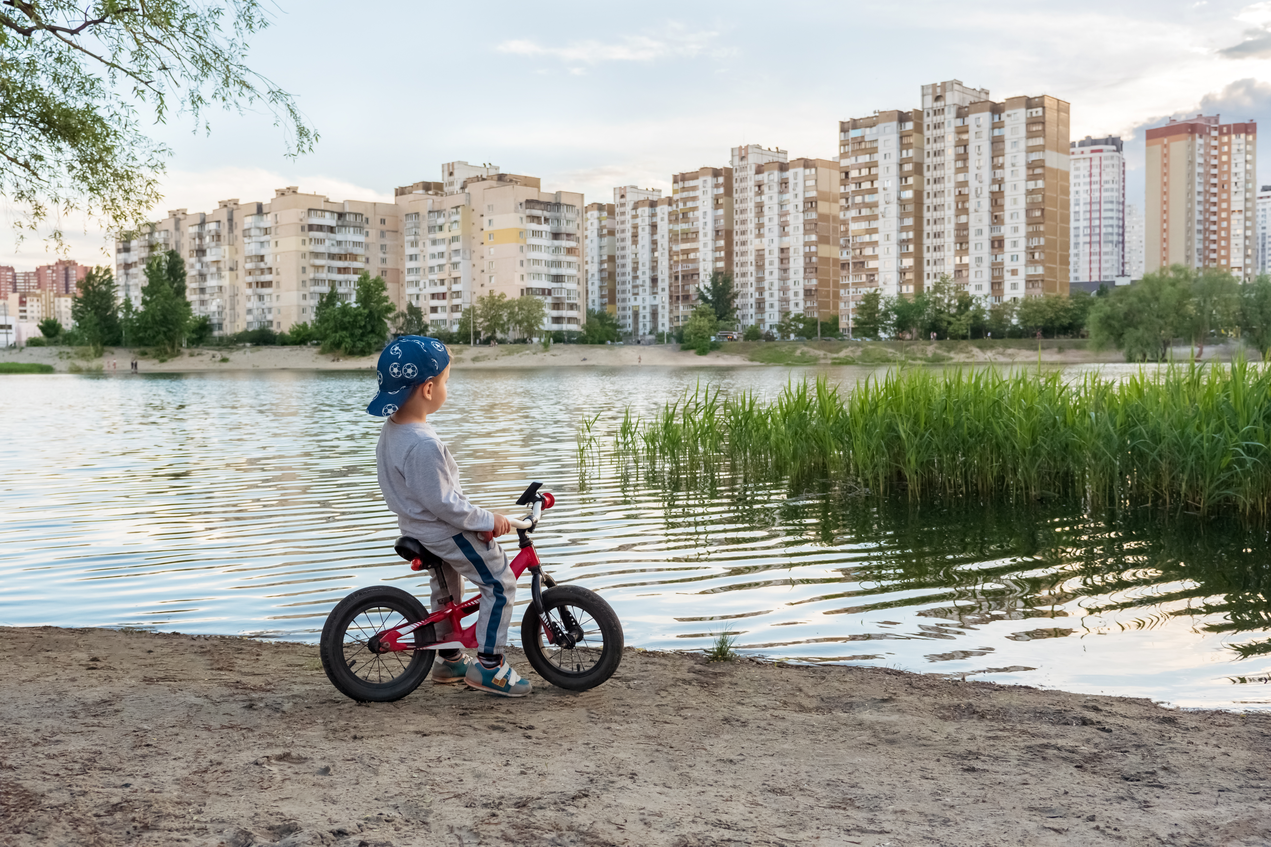 Boy on a bike looking over the water. Huge appartment blocks across the water. photo.