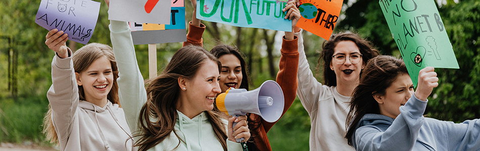 A group of people holding protest signs and a megaphone. The signs display messages related to environmental and animal rights, such as 'FOR ANIMALS', 'OUR FUTURE', and 'NO PLANET B'. Photo