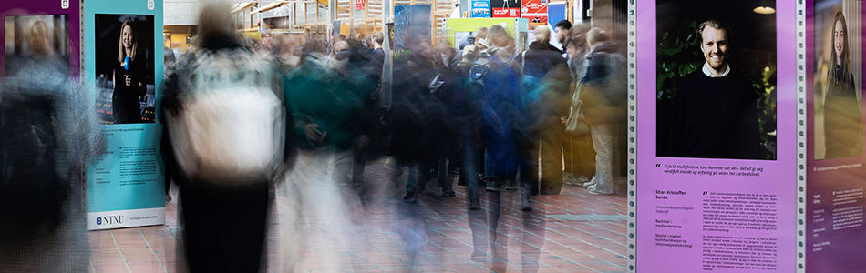A busy indoor hallway or exhibition area filled with people walking. Large informational posters line both sides of the hallway, displaying images and text about various individuals. The background is slightly blurred, emphasizing the movement and dynamic atmosphere of the scene. foto