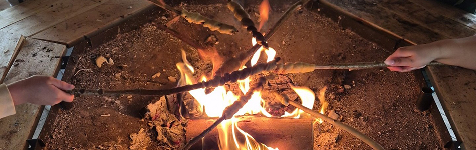 A bonfire with many sticks holding campfire bread being cooked over the fire. Photo.