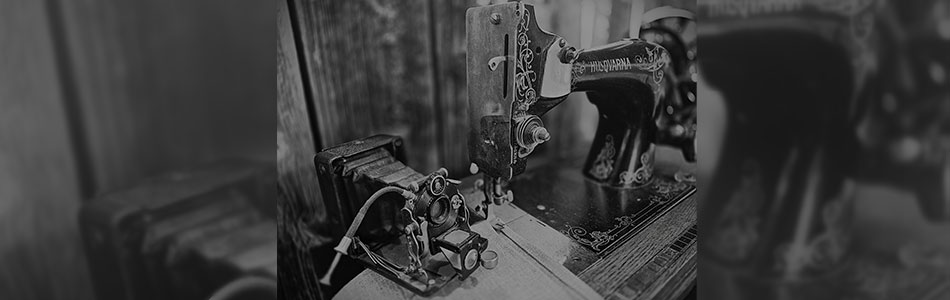 Close-up of an old mechanical sewing machine and a vintage camera on a wooden table, photographed in black and white. Photo.