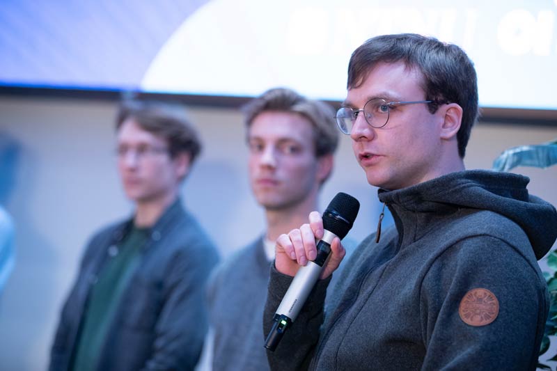 Photo of three students participating in a discussion panel. One of them holding a mic.