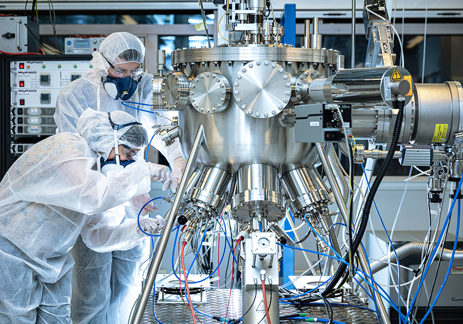 Two researchers in safety dress with instrument in the MBE lab. Photo