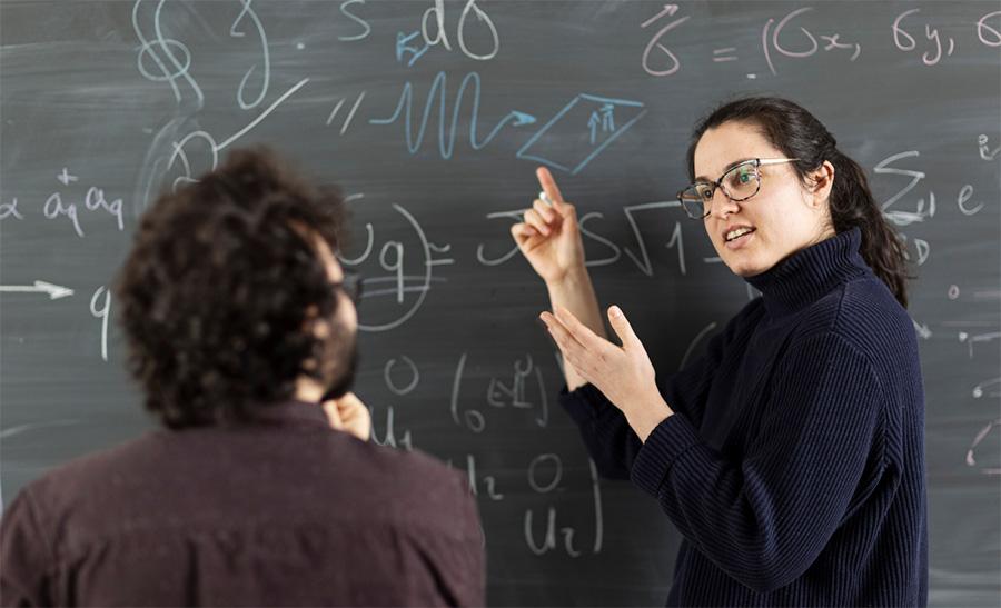 Researcher showing formula on the blackboard to another researcher. Photo