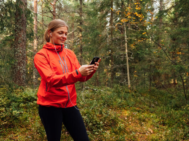 A woman, in workout gear, standing in the woods, looking at her smartphone