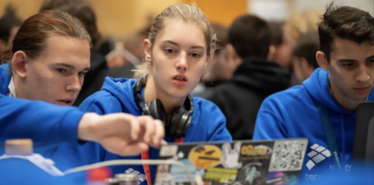 three students looking at computer screens. Dressed in blue sweatshirts