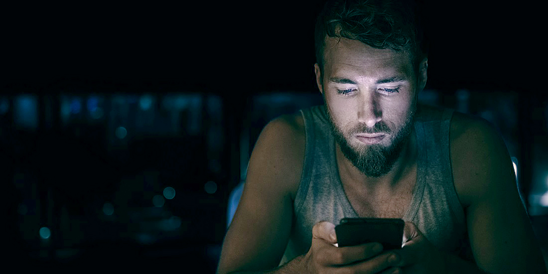 A man sitting in the dark, looking at his smartphone