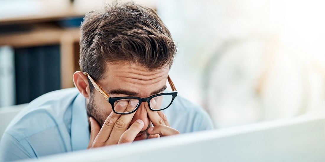 A man with a blue shirt holding his head, rubbing his eyes