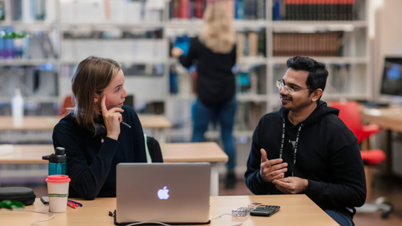 Two students talking to each other in front of a computer
