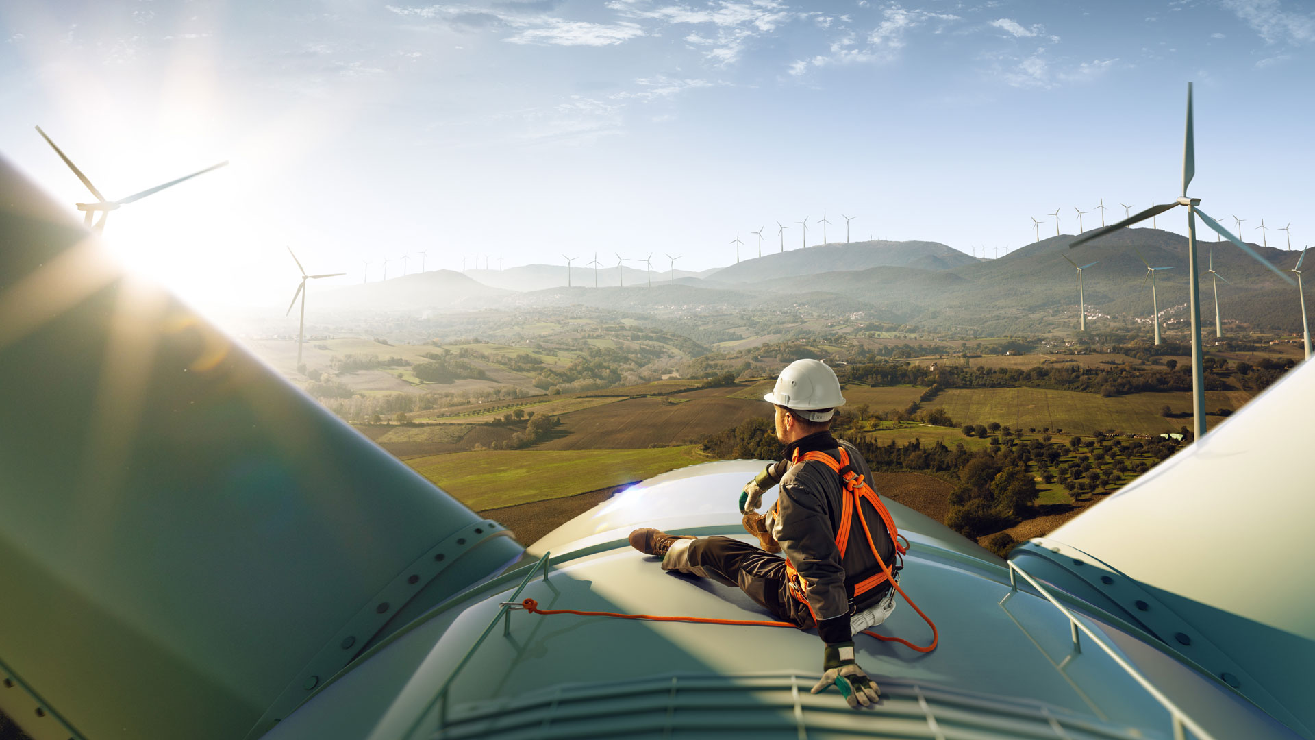 Man sitting on top of wind mill watching the sun and other wind mills