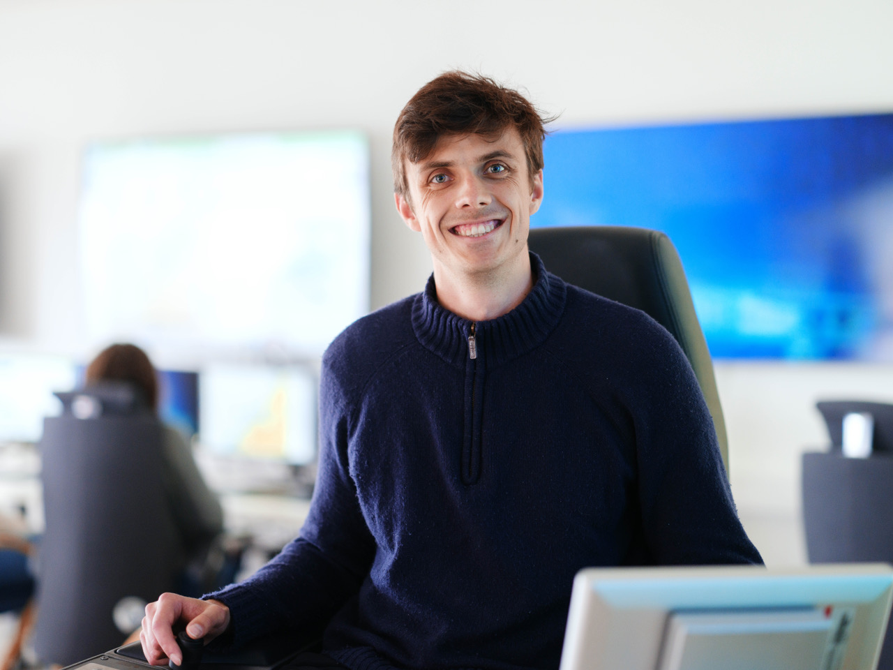 Smiling PhD in front of screens at AUR-Lab control room