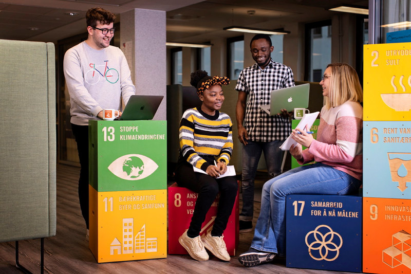 Fire studenter sitter på klosser med FNs bærekraftsmål. Foto