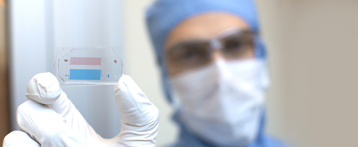 Researcher in the NanoLab holding up microfluidics equipment. Photo