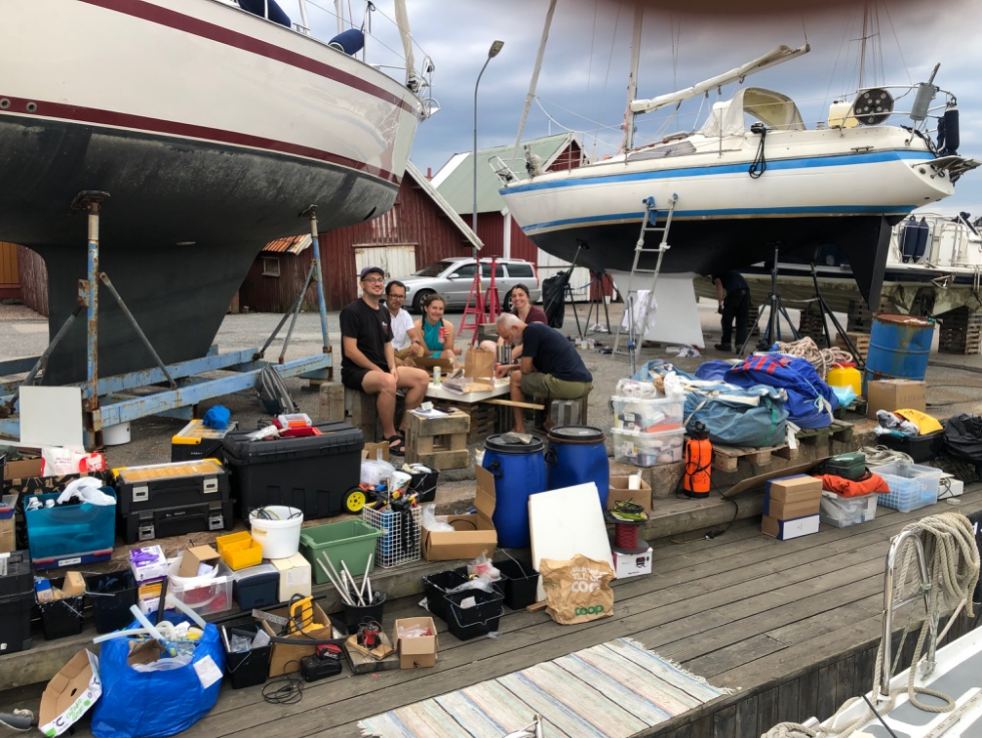 Part of the expedition team packing gear outside of the sailing vessel Hrimfare - five people on a harbor pier surrounded by a very large pile of organized equipment