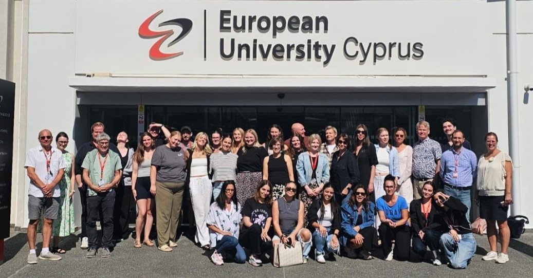 A group of people gathered in front of the entrance to European University Cyprus. Above the entrance is a large sign displaying the university’s name and logo. Photo