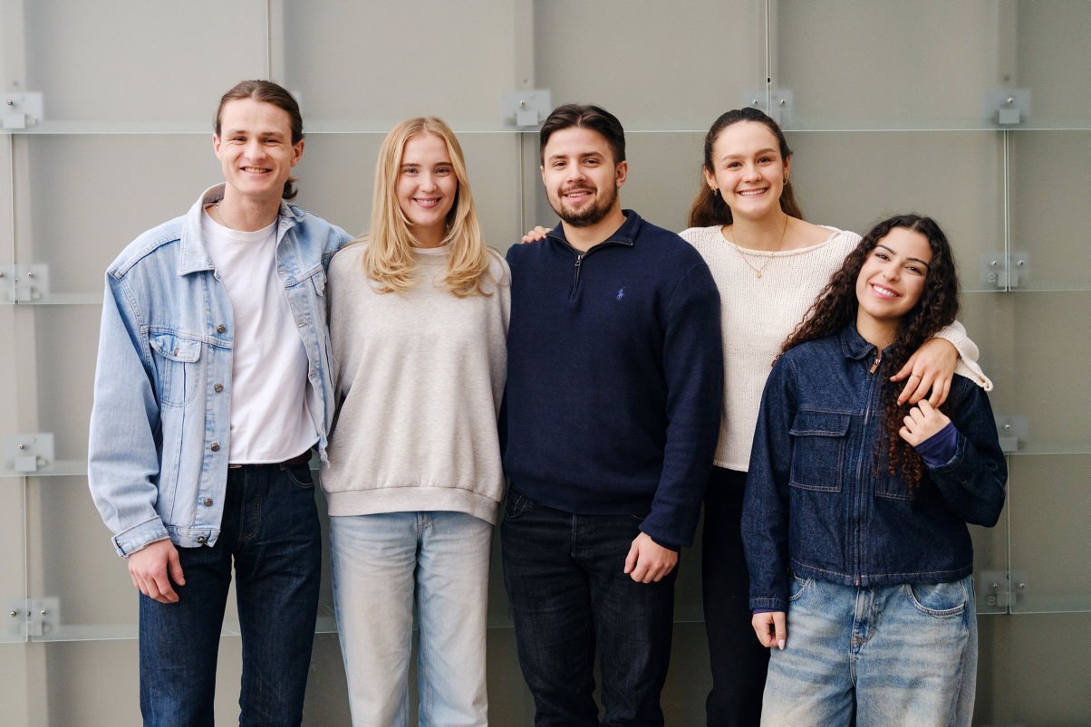 A group of students stand in a row smiling at the camera. Photo