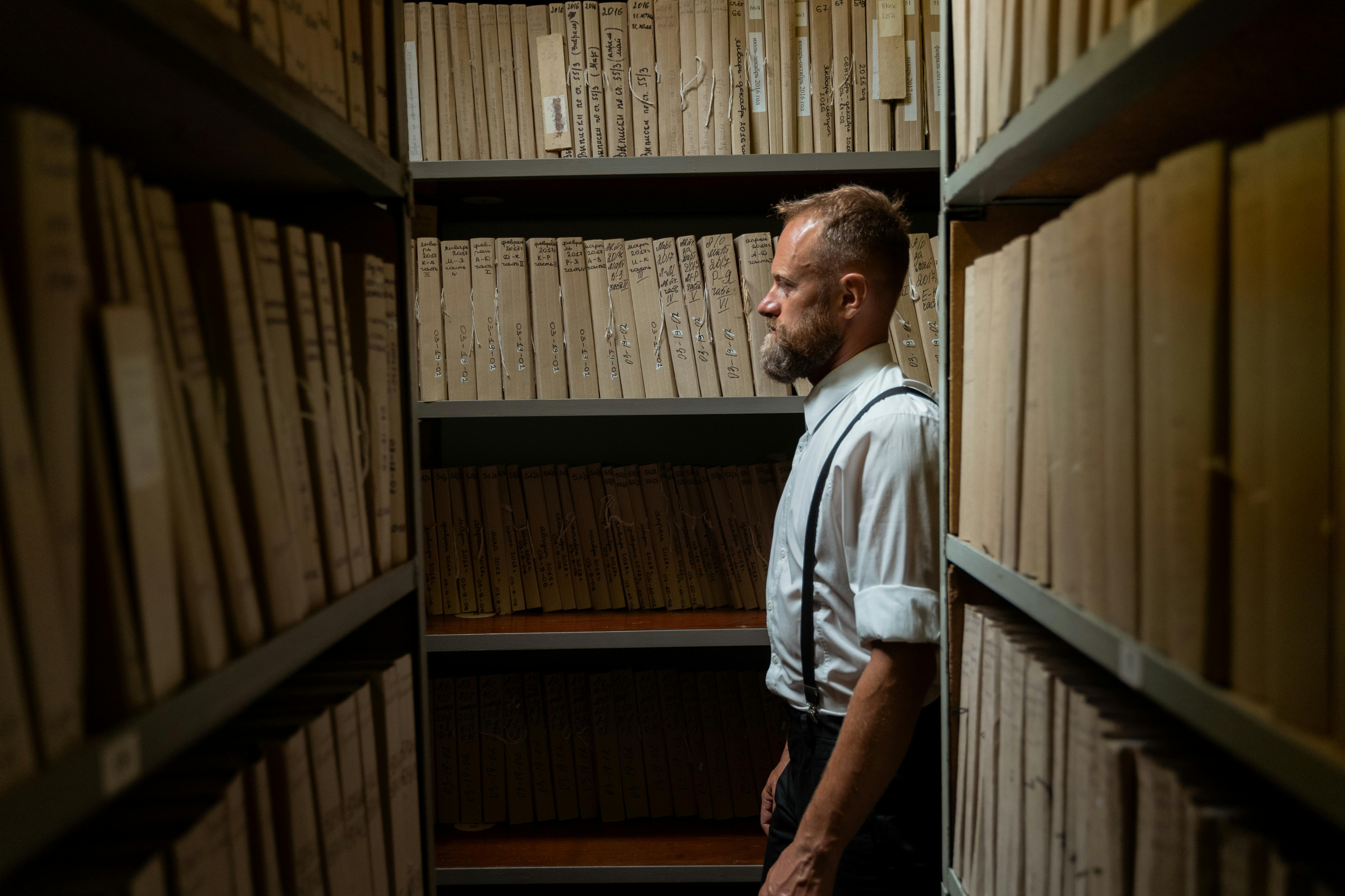 A man standing between bookshelves. Illustrative photo