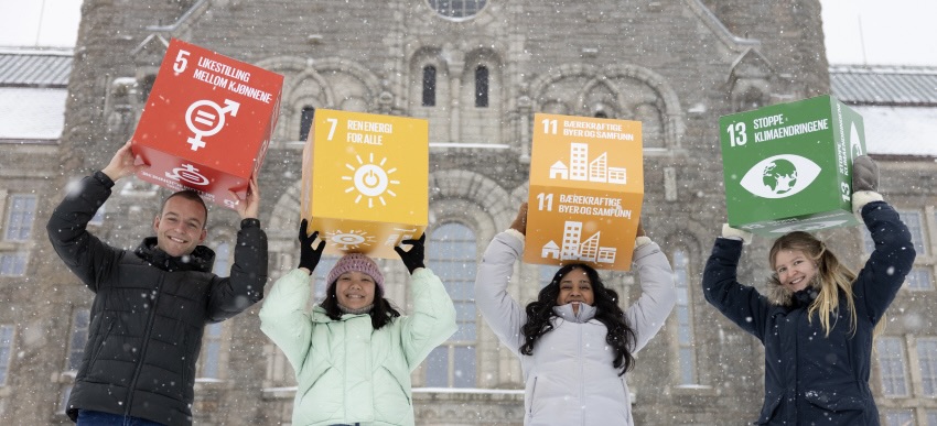 Four students in front of the NTNU main building - with some UN's goals for sustainable development
