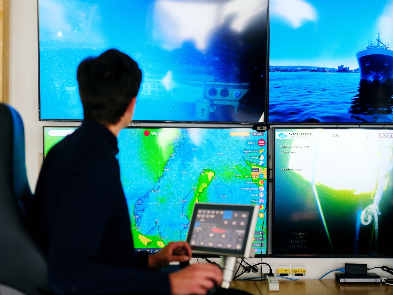 Man in front of four screens in a control room