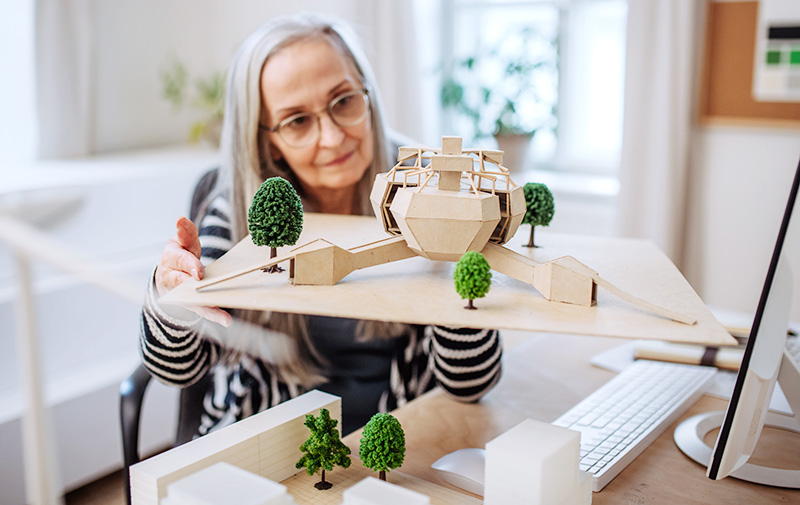 An older woman looking at a model of a building with trees. Photo