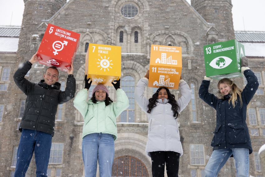 Four students in front of the main building at Gløshaugen