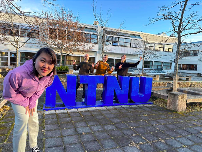 Somat participants standing by NTNU sign on campus yard