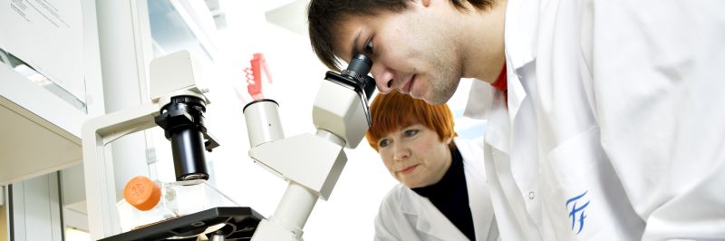 Two persons in a lab looking in a microscope