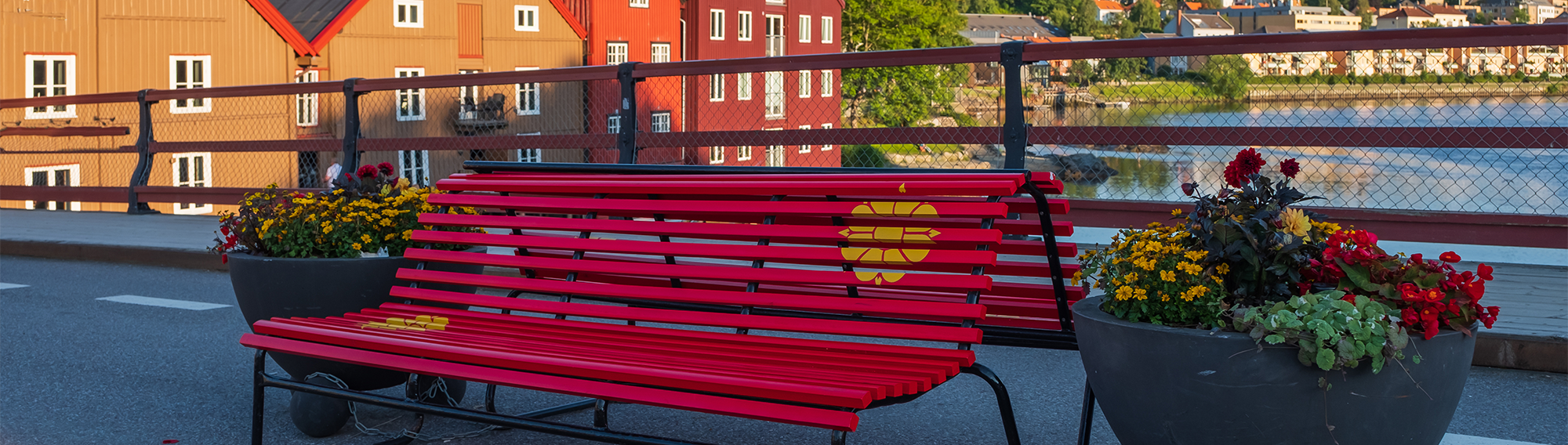 Red bench on a bridge with flowers. Colourful wharf houses along the river in the background.