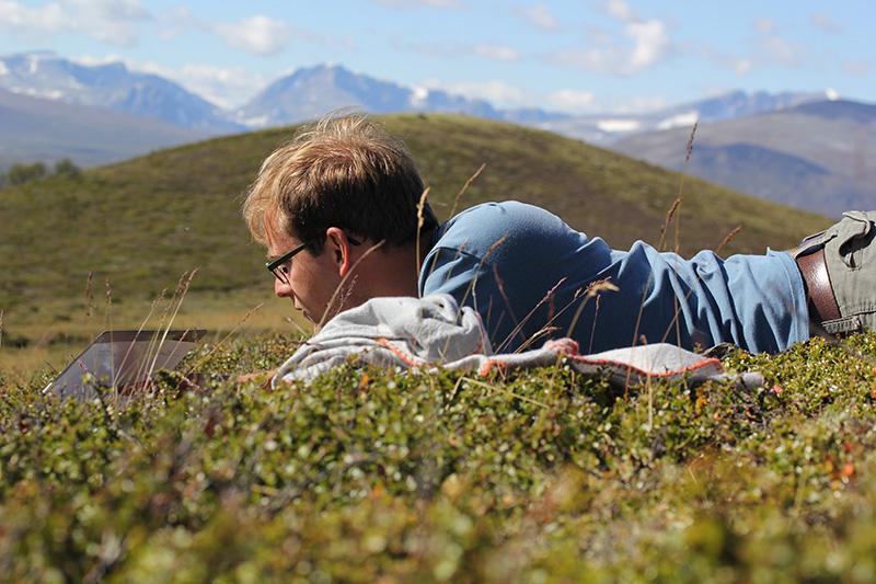 Researcher laying down working on computer on the tundra. Photo