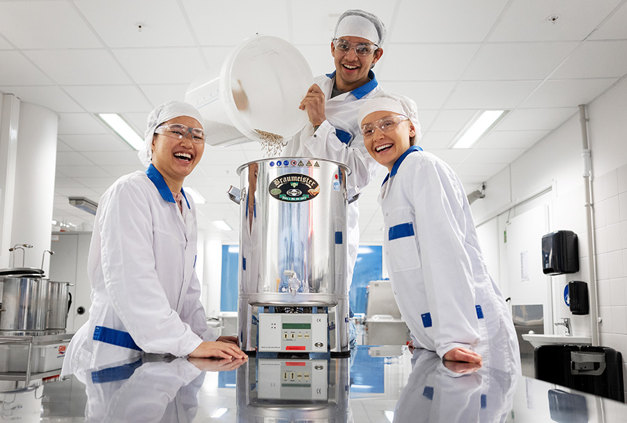Three students with safety clothing in a laboratory working with a big pot