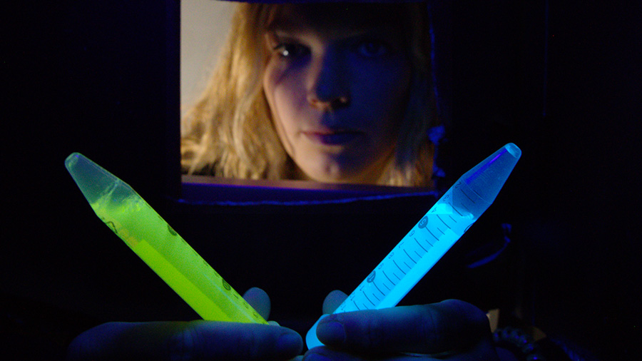 Two tubes with glow in the dark fluid in a dark room with a researcher
