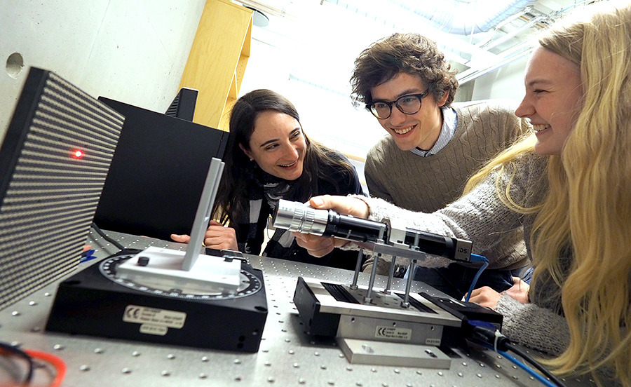Three researchers in the lab. One researcher is holding a laser. Photo