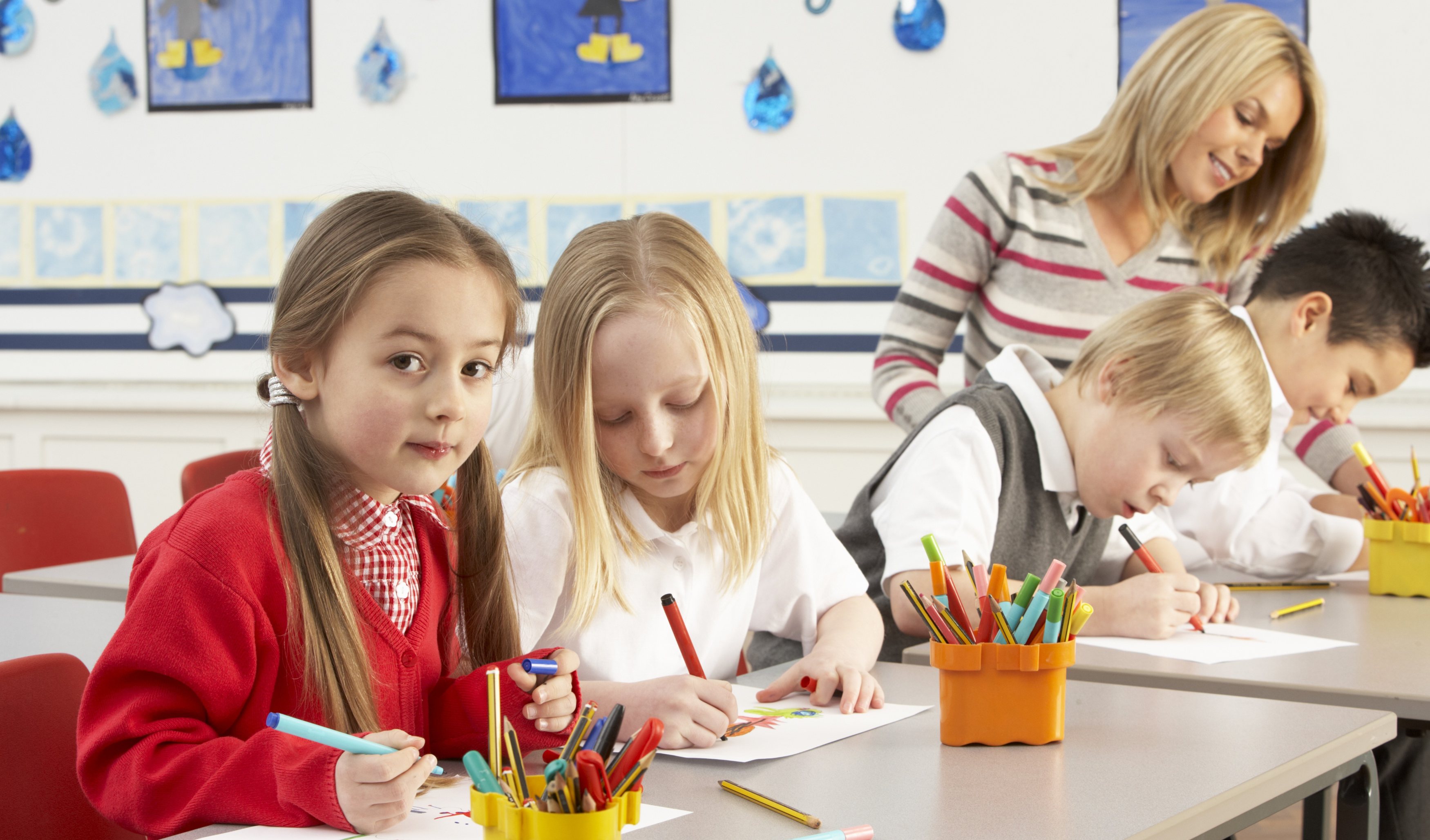 Young students drawing, while teacher is looking at the pictures