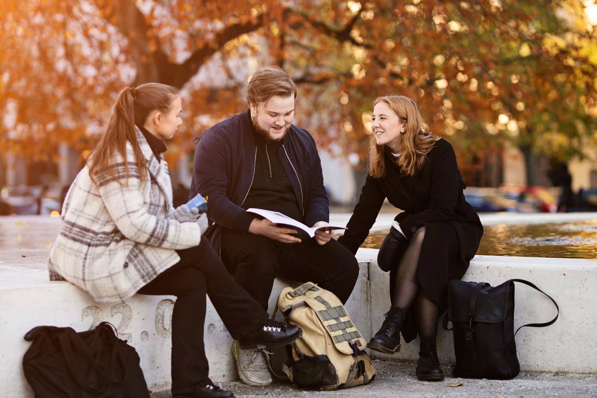 A group of people reading a book next to a fountain. Photo.