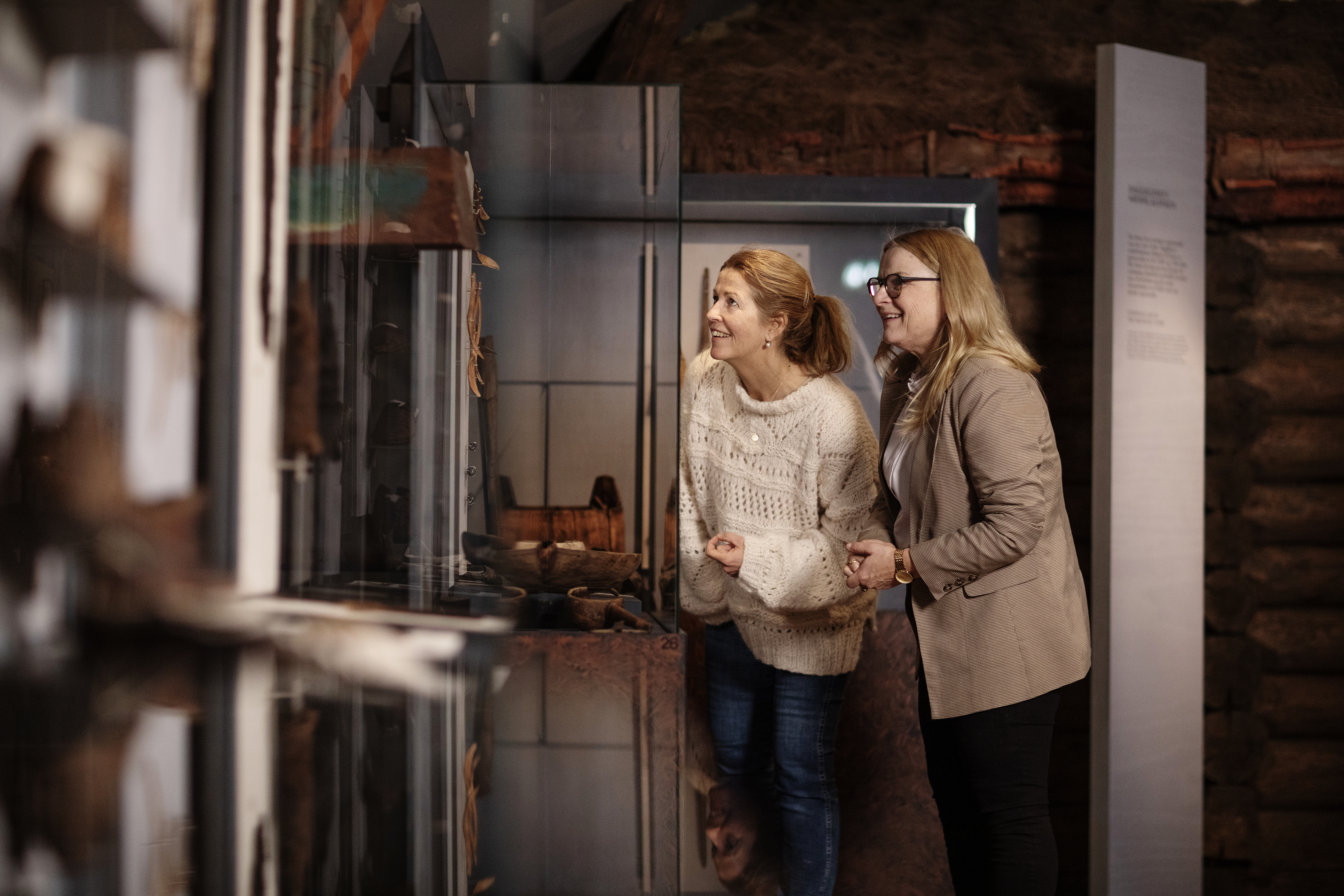 Two smiling women looking into a glass case.