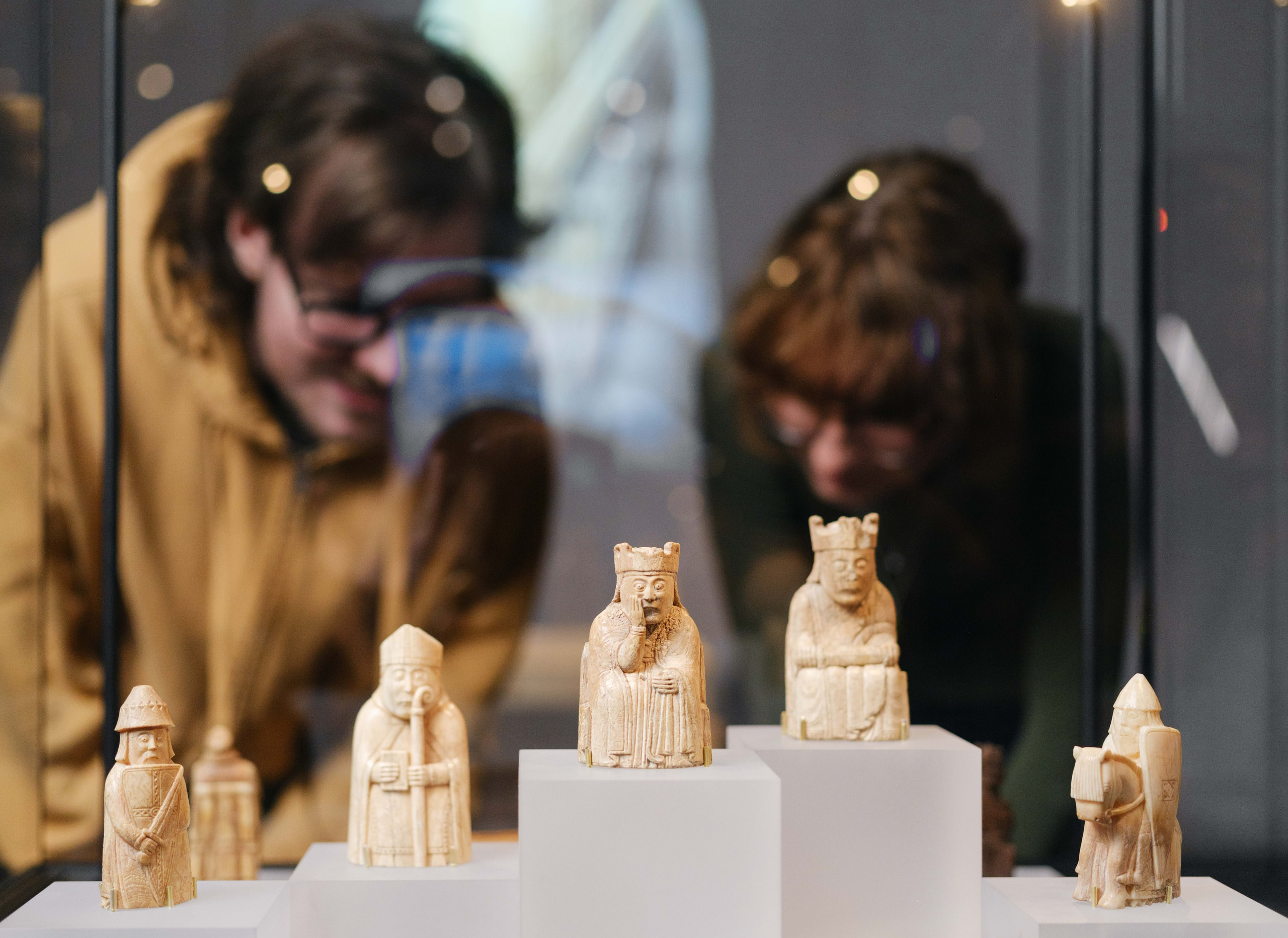 A young man and a young woman are looking at a display of the Lewis chess pieces.