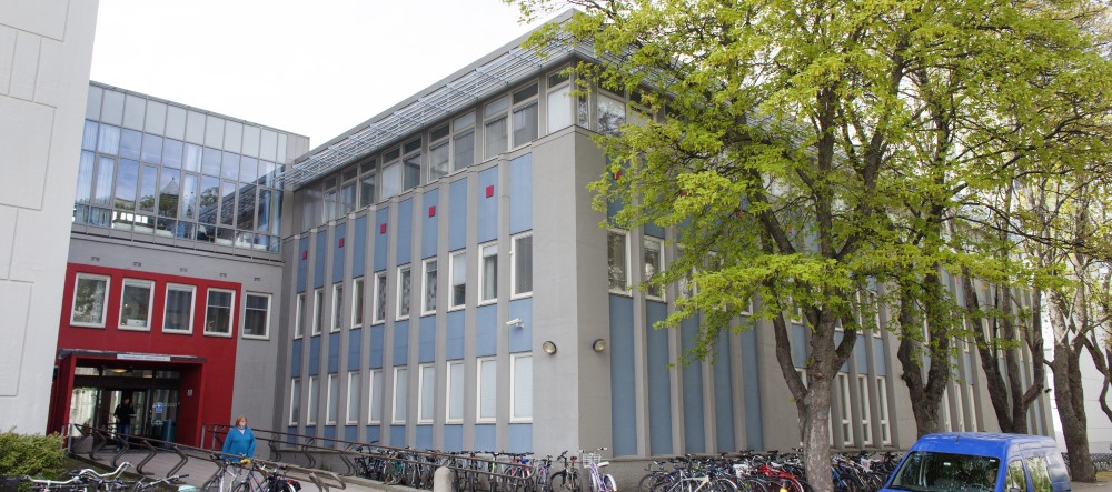 Gray and light blue building in which the library is locatated on the top floor. The ground floor entrance is framed in red. Photo.