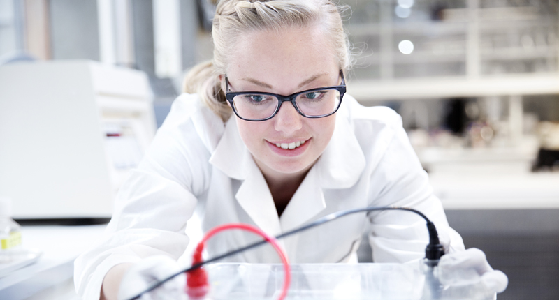 Female student in lab coat is smiling. Photo